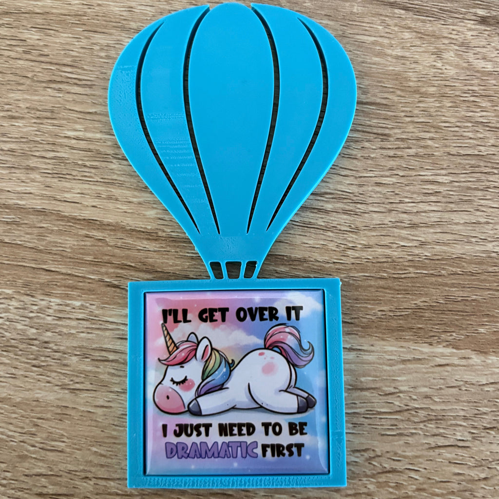 Blue hot air balloon with a humorous card featuring a unicorn on a wooden surface